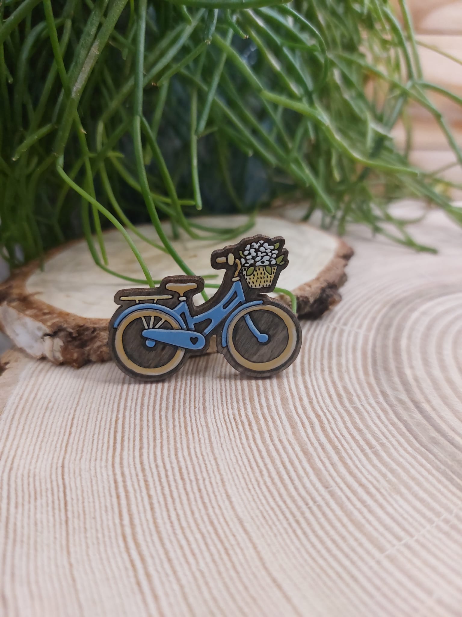 Na zdjęciu widać drewnianą, ręcznie malowaną broszkę z motywem roweru.