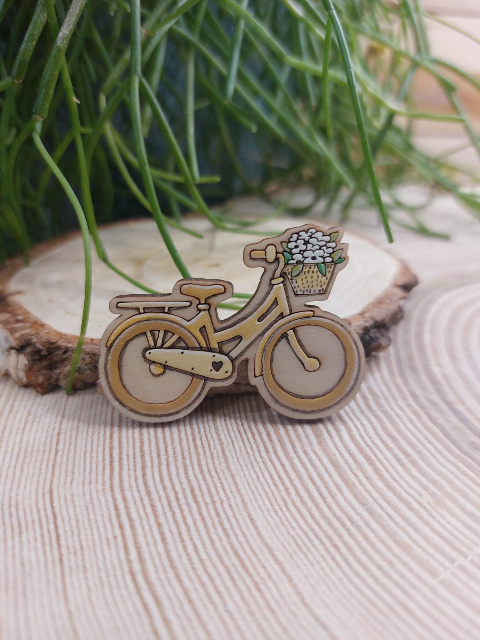 Na zdjęciu widać drewnianą, ręcznie malowaną broszkę z motywem roweru.