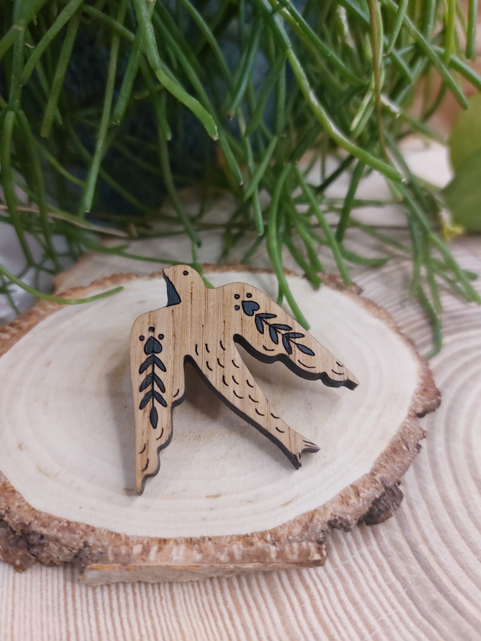 Na zdjęciu widać drewnianą, ręcznie malowaną broszkę z motywem jaskółki.